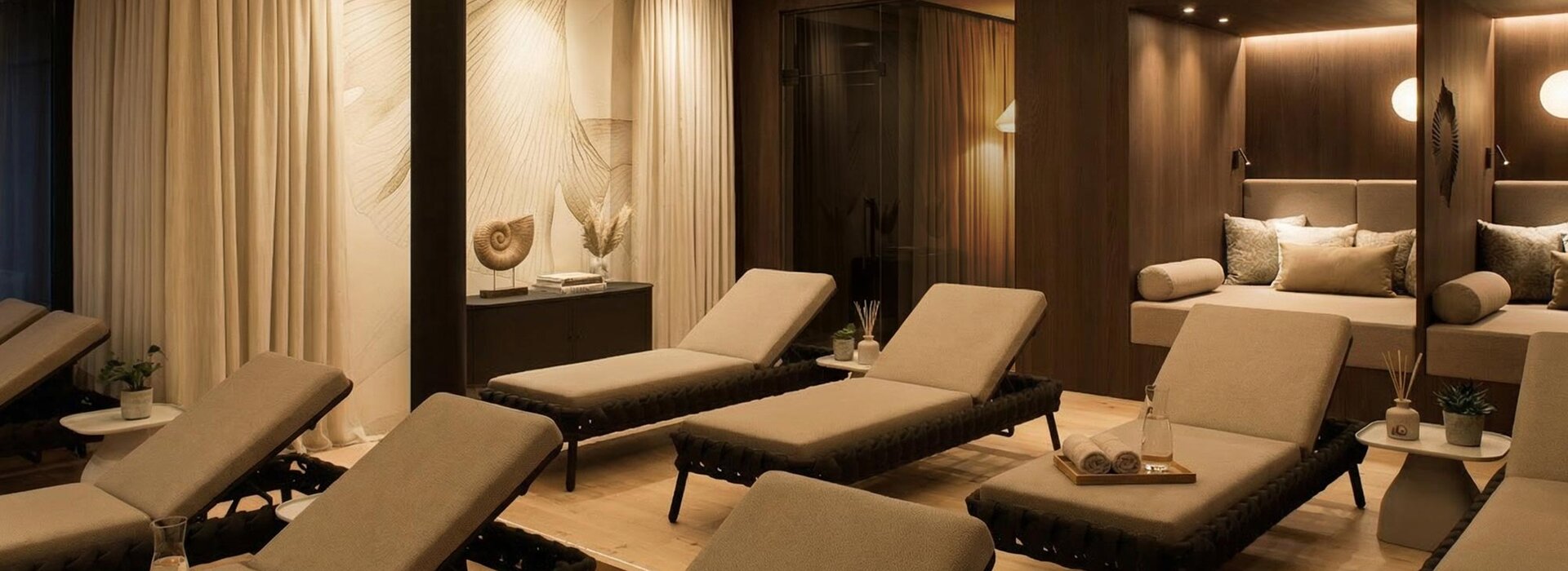 Eine ruhiger Ruheraum mit gepolsterten Liegestühlen, gedämpfter Beleuchtung und neutralem Dekor. Aufgerollte Handtücher, Wassergläser befinden sich auf den Liegen und kleine Pflanzen stehen auf Beistelltischen und schaffen eine ruhige und einladende Atmosphäre.
