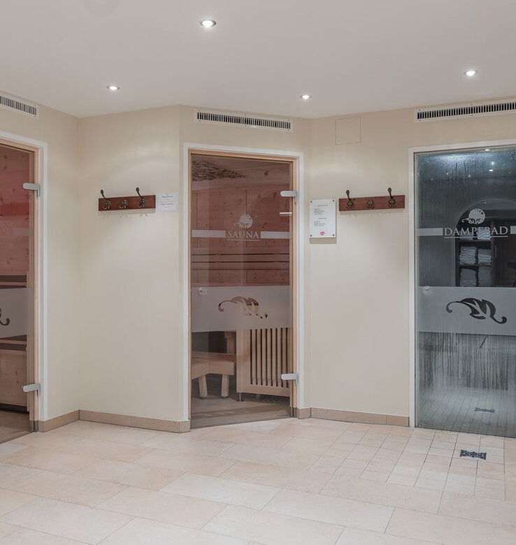 Drei moderne Spa-Räume mit Glastüren mit der Aufschrift "Sauna", "Infrarot" und "Dampfbad". Jede Tür ist mit einer Milchglasscheibe und dekorativen Mustern versehen. Der Bereich ist sauber und gut beleuchtet, auf der rechten Seite steht eine Vase mit roten Blumen.