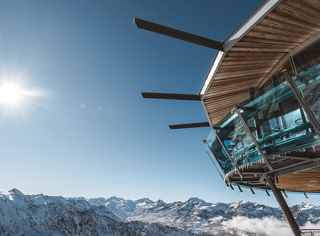 Ein modernes Glasgebäude mit Blick auf schneebedeckte Berggipfel unter einem strahlend blauen Himmel und strahlendem Sonnenschein.