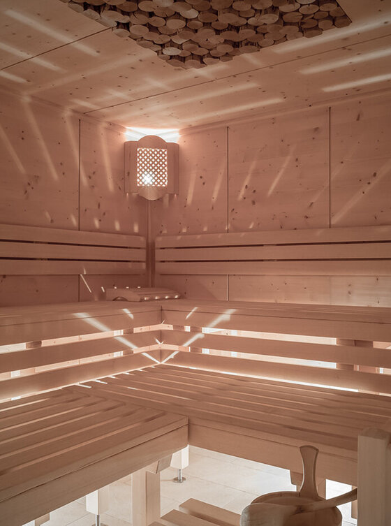 Innenraum der Holzsauna mit Bänken, einer Uhr an der Wand und Lichter, die ein Muster durch die Sauna werfen.