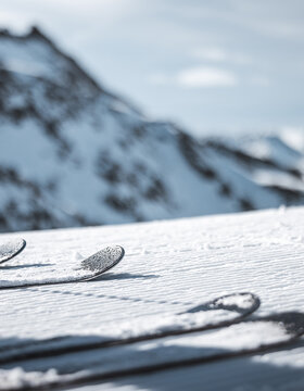 Die Skier ruhen auf dem präparierten Schnee, während die verschneiten Berggipfel im Hintergrund verschwimmen.