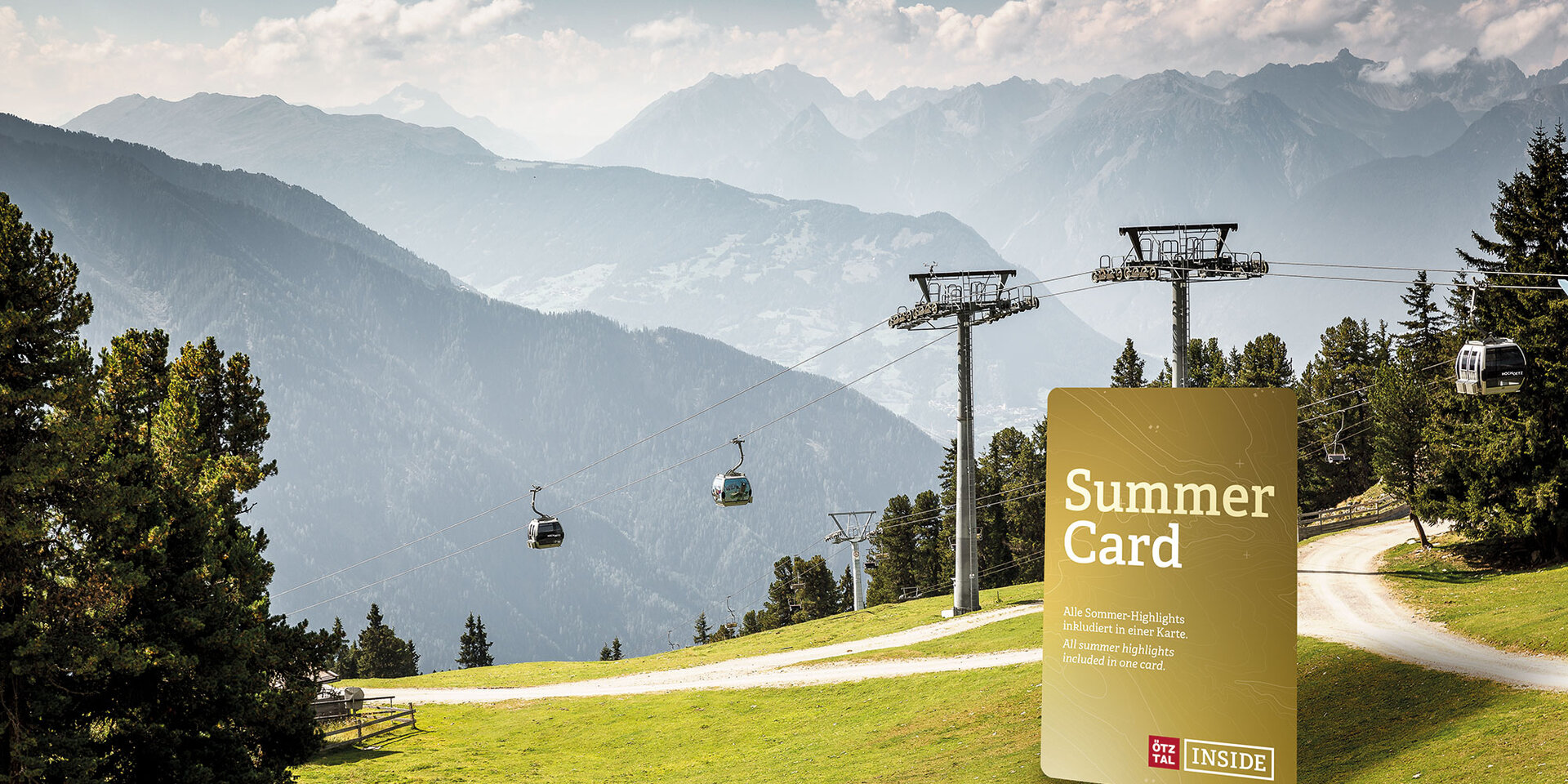 Seilbahnen führen durch eine grüne Berglandschaft unter einem teilweise bewölkten Himmel. Zu sehen ist eine große Sommercard-Schild Grafik im Vordergrund.