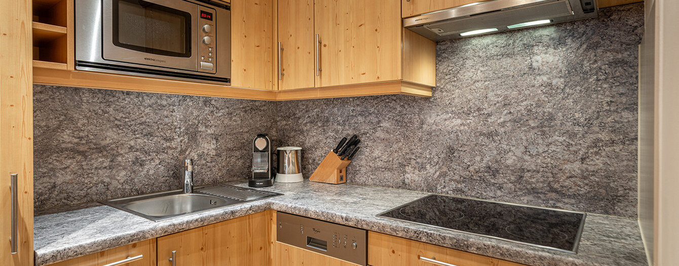 Eine moderne Küche mit hellen Holzschränken, grauen Steinarbeitsplatten und Backsplash, einer eingebauten Mikrowelle, einem Induktionskochfeld, einer Spüle, einer Kaffeemaschine, einem Messerblock und einer Unterschrankbeleuchtung.