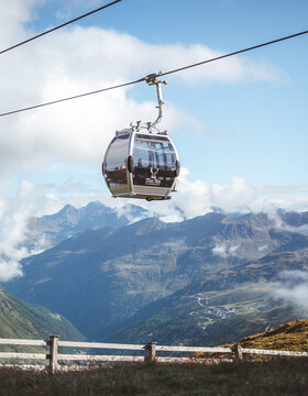 Eine Seilbahn fährt über grüne Berge und Täler unter einem blauen Himmel mit Wolken.